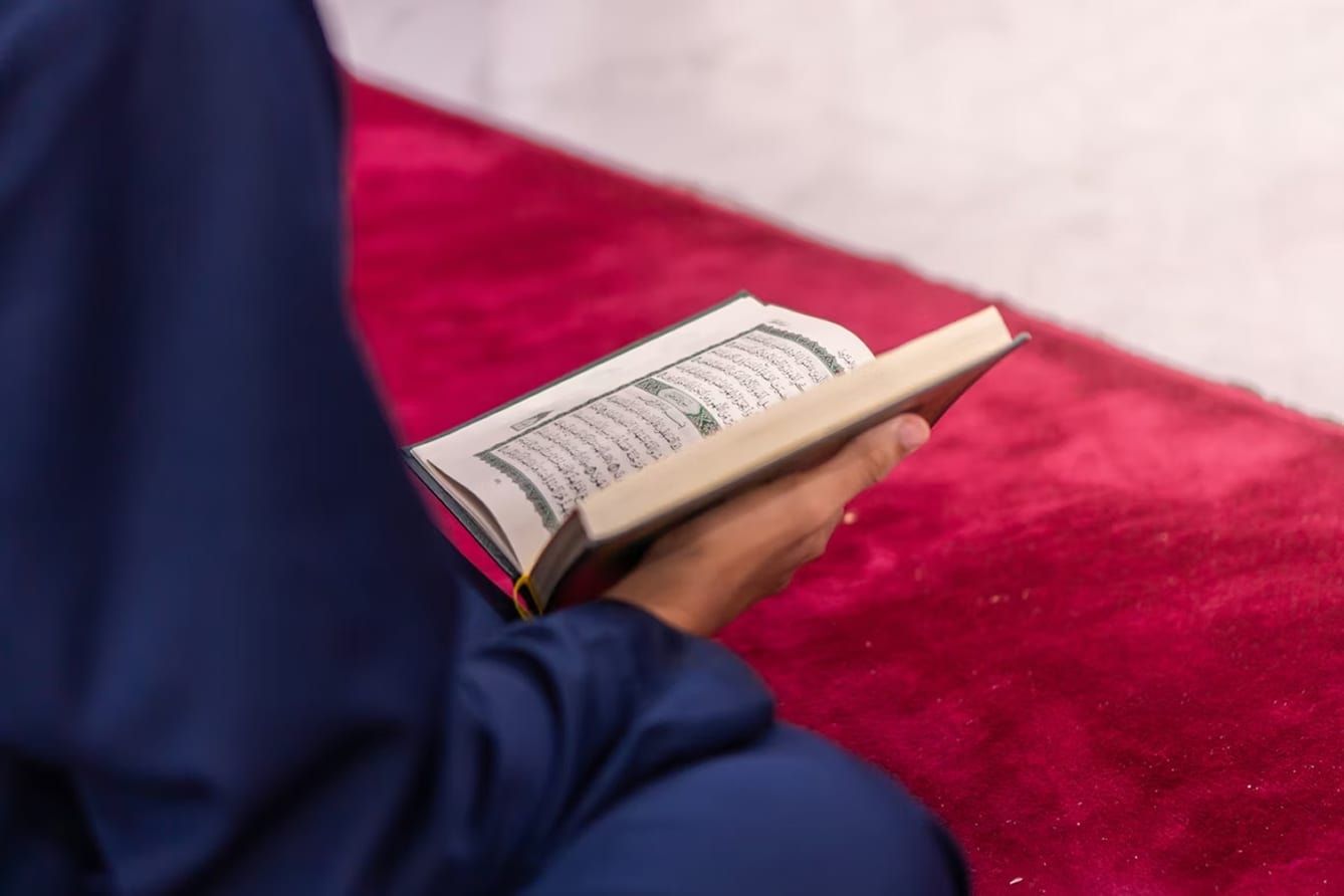 An open Qur'an resting on a patterned prayer mat